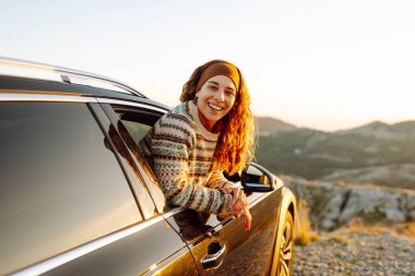 Güzel bir kadının arabanın yanında dikilip günbatımının tadını çıkardığı arka manzara. Yaşam tarzı, seyahat, turizm, doğa, aktif yaşam.