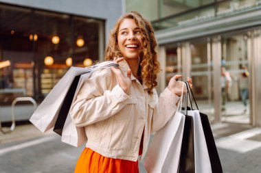 Şehir caddesinde alışveriş torbalarıyla yürüyen güzel bir genç kadının portresi. Tüketim, satış, alım, alışveriş, yaşam tarzı konsepti.