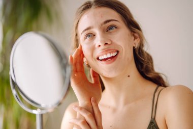 Derisi sorunlu genç bir kadın aynaya bakıyor. Sivilce terapisi kavramı, yara izleri, yüzünde iltihap, sorunlu cilt. Güzellik bakımı.