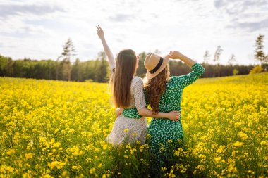 Çiçek açan bir tarlada iki güzel kadının portresi. Doğa, tatil, rahatlama ve yaşam tarzı. Yaz manzarası.