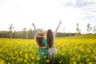 Çiçek açan bir tarlada iki güzel kadının portresi. Doğa, tatil, rahatlama ve yaşam tarzı. Yaz manzarası.
