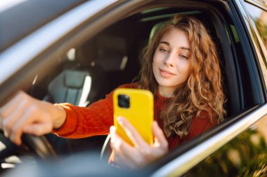 Arabada cep telefonu kullanan genç bir kadın. Boş zaman, seyahat, teknoloji. Araba paylaşımı.