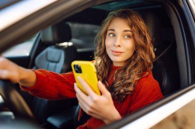 Arabada cep telefonu kullanan genç bir kadın. Boş zaman, seyahat, teknoloji. Araba paylaşımı.