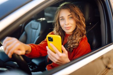 Arabada cep telefonu kullanan genç bir kadın. Boş zaman, seyahat, teknoloji. Araba paylaşımı.