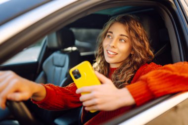 Arabada cep telefonu kullanan genç bir kadın. Boş zaman, seyahat, teknoloji. Araba paylaşımı.