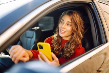 Arabada cep telefonu kullanan genç bir kadın. Boş zaman, seyahat, teknoloji. Araba paylaşımı.