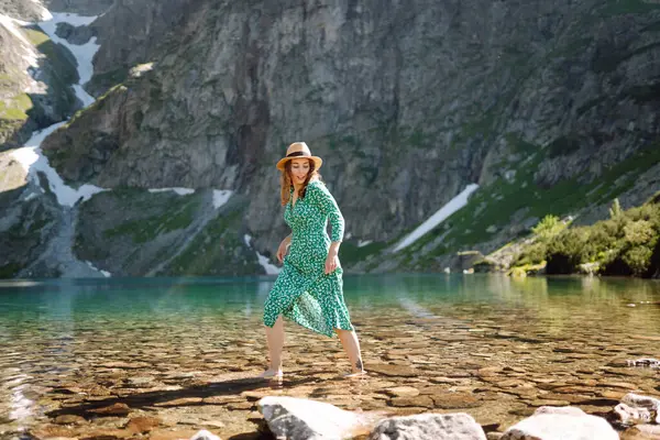 Yazlık elbiseli bir turist dağ gölüne bakarak doğanın güzelliğinin tadını çıkarıyor. Yaşam tarzı, moda, seyahat kavramı.