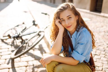 Sokak şehrinde bisikletin yanında oturan gülümseyen kadının portresi. Seyahat, hafta sonu, rahatlama ve yaşam tarzı konsepti. Eko taşımacılığı.