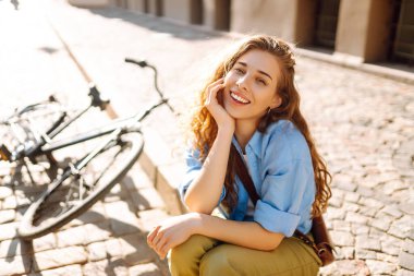 Sokak şehrinde bisikletin yanında oturan gülümseyen kadının portresi. Seyahat, hafta sonu, rahatlama ve yaşam tarzı konsepti. Eko taşımacılığı.