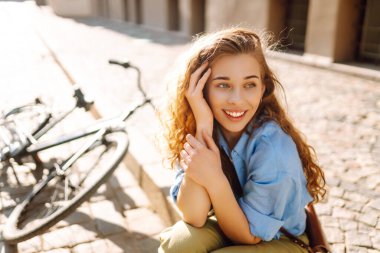 Sokak şehrinde bisikletin yanında oturan gülümseyen kadının portresi. Seyahat, hafta sonu, rahatlama ve yaşam tarzı konsepti. Eko taşımacılığı.