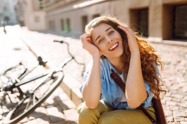 Sokak şehrinde bisikletin yanında oturan gülümseyen kadının portresi. Seyahat, hafta sonu, rahatlama ve yaşam tarzı konsepti. Eko taşımacılığı.