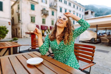 Mutlu kadın yaz güneşli bir günde, açık hava kaldırım kafe restoranının kahvesini yudumluyor. İnsanlar, moda, yaşam tarzı, seyahat ve tatiller
