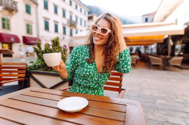 Mutlu kadın yaz güneşli bir günde, açık hava kaldırım kafe restoranının kahvesini yudumluyor. İnsanlar, moda, yaşam tarzı, seyahat ve tatiller
