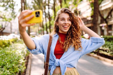 Güzel bir kadın cep telefonuyla sokaklarda dolaşıyor ve selfie çekiyor. Seyahat, blog, hafta sonu, rahatlama ve yaşam tarzı konsepti.