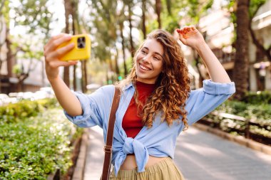 Güzel bir kadın cep telefonuyla sokaklarda dolaşıyor ve selfie çekiyor. Seyahat, blog, hafta sonu, rahatlama ve yaşam tarzı konsepti.