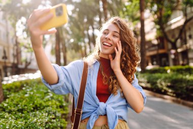 Güzel bir kadın cep telefonuyla sokaklarda dolaşıyor ve selfie çekiyor. Seyahat, blog, hafta sonu, rahatlama ve yaşam tarzı konsepti.