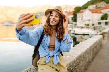 Şehrin ve körfezin arka planında selfie çeken genç bir kadın. Seyahat, turizm, teknoloji, blog, iletişim kavramı.
