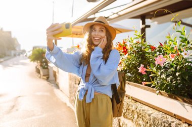 Şehrin ve körfezin arka planında selfie çeken genç bir kadın. Seyahat, turizm, teknoloji, blog, iletişim kavramı.