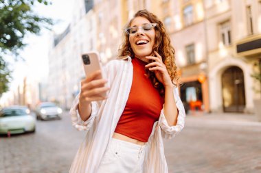 Genç kadın turist sokakta yürüyor, selfie çekiyor, arkadaşlarıyla iletişim kuruyor. Ağlar, bloglar, online alışveriş kavramı.