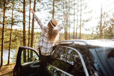 Genç bayan turistin arkası dinleniyor ve arabanın yanındaki yolculuğun tadını çıkarıyor. Seyahat macerası, mutlu yaz..