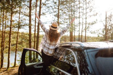 Genç bayan turistin arkası dinleniyor ve arabanın yanındaki yolculuğun tadını çıkarıyor. Seyahat macerası, mutlu yaz..