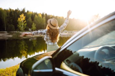 Genç bayan turistin arkası dinleniyor ve arabanın yanındaki yolculuğun tadını çıkarıyor. Seyahat macerası, mutlu yaz..
