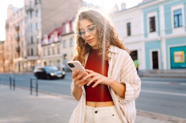 Gülümseyen genç bir kadın eski caddede yürüyor, selfie çekiyor, arkadaşlarla iletişim kuruyor. Ağlar, bloglar, online alışveriş kavramı.