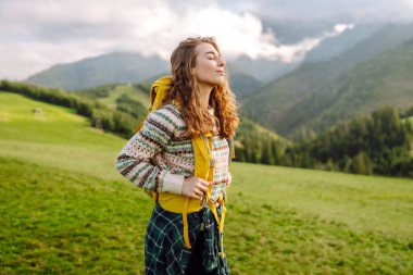 Güneşli bir günde, yeşil çimen tarlasında yürüyen kadın turist. Güzel dağlar manzarası.