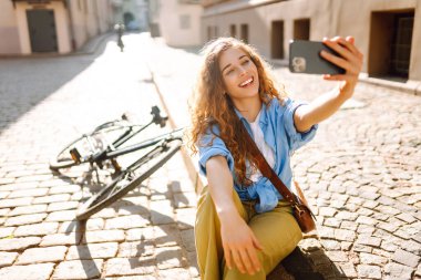 Selfie zamanı. Bisikletle yürüyüp güzel bir mimariye bakarken cep telefonu kullanan mutlu bir kadın. İnsanlar, boş zaman, blog ve yaşam tarzı.