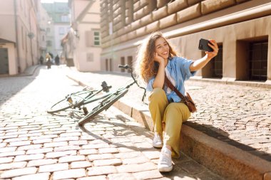 Selfie zamanı. Bisikletle yürüyüp güzel bir mimariye bakarken cep telefonu kullanan mutlu bir kadın. İnsanlar, boş zaman, blog ve yaşam tarzı.