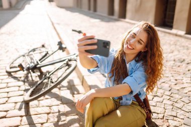 Selfie zamanı. Bisikletle yürüyüp güzel bir mimariye bakarken cep telefonu kullanan mutlu bir kadın. İnsanlar, boş zaman, blog ve yaşam tarzı.