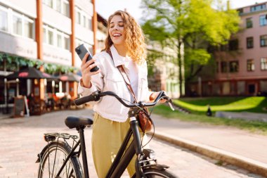 Bisikletle yürürken cep telefonu kullanan genç bir kadın güzel bir mimariye bakıyor. Selfie zamanı. İnsanlar, boş zaman, blog ve yaşam tarzı.