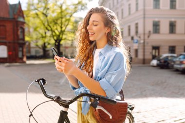 Bisikletle yürürken cep telefonu kullanan genç bir kadın güzel bir mimariye bakıyor. Selfie zamanı. İnsanlar, boş zaman, blog ve yaşam tarzı.