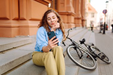 Bisikletle yürürken cep telefonu kullanan genç bir kadın güzel bir mimariye bakıyor. Selfie zamanı. İnsanlar, boş zaman, blog ve yaşam tarzı.