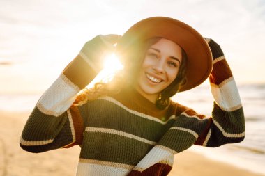 Şık bir kadın serin bir günde deniz ya da okyanus sahillerinde günbatımında yürür. Harika bir açık hava manzarası. Seyahat, hafta sonu, rahatlama ve yaşam tarzı konsepti.