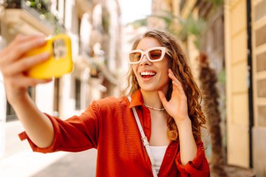 Avrupa sokaklarında yürüyüp selfie çeken mutlu bir turist kadın. Seyahat, turizm, teknoloji, blog, iletişim kavramı.