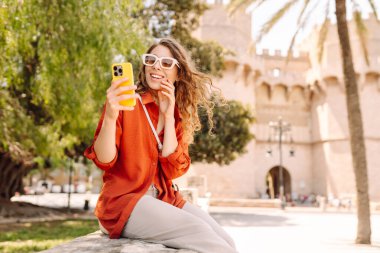 Avrupa sokaklarında yürüyüp selfie çeken mutlu bir turist kadın. Seyahat, turizm, teknoloji, blog, iletişim kavramı.