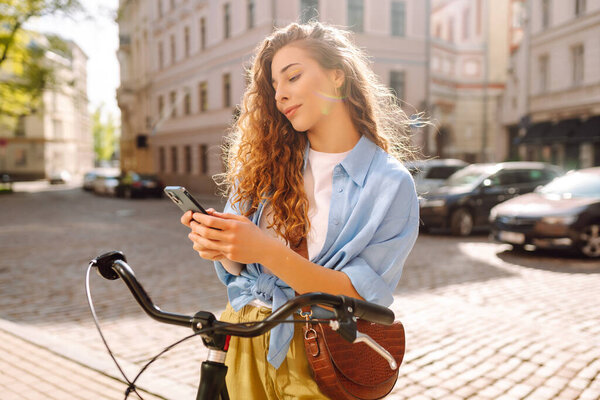 Молодая женщина использует мобильный телефон во время прогулок на велосипеде и смотрит вокруг на красивую архитектуру. Время селфи. Люди, отдых, блоги и образ жизни.