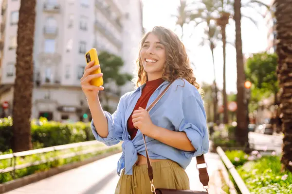 Sokak şehrinde cep telefonu olan bir kadın gezgin. Genç bir kadın güneşli bir günde mesajlaşıyor, göz gezdiriyor, akıllı telefonunu kullanıyor. İş, teknoloji, blog, iletişim kavramı.