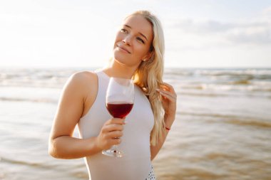 Gün batımında zarif beyaz elbiseler içinde bir bardak şarapla güzel bir manken. Seyahat, hafta sonu, rahatlama ve yaşam tarzı konsepti.