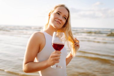 Gün batımında zarif beyaz elbiseler içinde bir bardak şarapla güzel bir manken. Seyahat, hafta sonu, rahatlama ve yaşam tarzı konsepti.