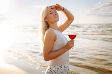 Gün batımında zarif beyaz elbiseler içinde bir bardak şarapla güzel bir manken. Seyahat, hafta sonu, rahatlama ve yaşam tarzı konsepti.