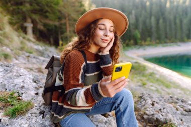 Genç bayan turist doğada akıllı telefon kullanıyor. Yürüyüş, spor, seyahat ve teknoloji konsepti.