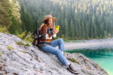 Genç bayan turist doğada akıllı telefon kullanıyor. Yürüyüş, spor, seyahat ve teknoloji konsepti.