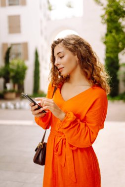 Sokakta dolaşan genç bir kadın akıllı telefon kullanıyor, arkadaşlarıyla iletişim kuruyor. Ağlar, bloglar, online alışveriş kavramı.