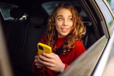Arabada akıllı telefon kullanan mutlu genç bir kadın. Teknoloji kavramı, blog yazma, arabayla seyahat, iş.