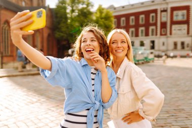 İki modaya uygun kadın şehir merkezini ziyaret ediyor ve akıllı telefondan şehir simgelerinin fotoğraflarını çekiyor. Moda, seyahat, blog, teknoloji kavramı