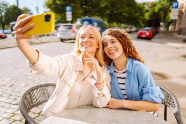 Kafede oturan mutlu güzel kızlar kamerayla selfie çeker. Moda, güzellik, blog, turizm.