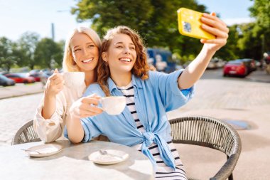 Kafede oturan mutlu güzel kızlar kamerayla selfie çeker. Moda, güzellik, blog, turizm.