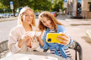 Kafede oturan mutlu güzel kızlar kamerayla selfie çeker. Moda, güzellik, blog, turizm.